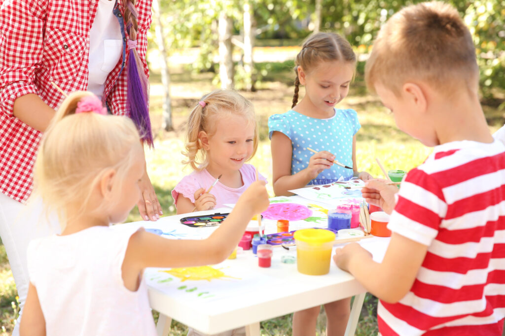 Kids sitting around an outdoor table doing crafts - Kids Outside Adventures