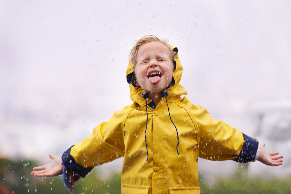 Child in yellow raincoat standing in the rain with tongue sticking out - Rainy Day Activities for Families - Rainy Day Activities for Families - Kids Outside Adventures