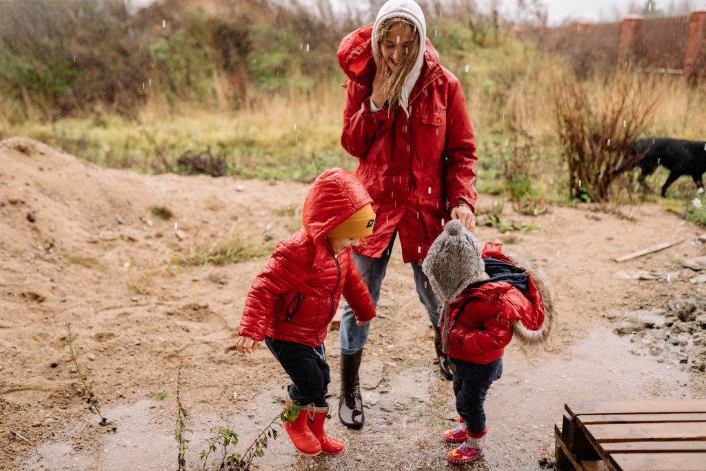 Mom and two kids in red raincoats playing outside in a puddle - Rainy Day Activities for Families - Kids Outside Adventures